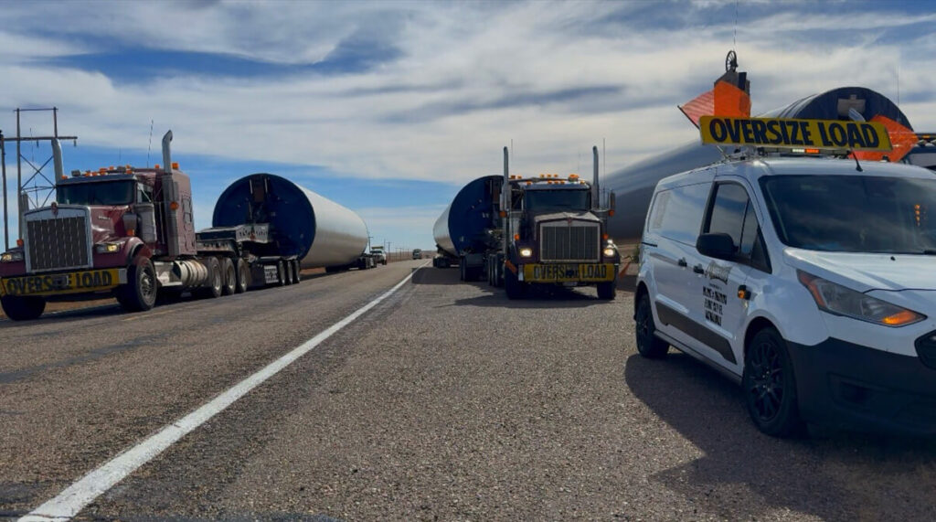 pilot car in front, semi truck with heavy load behind the pilot car