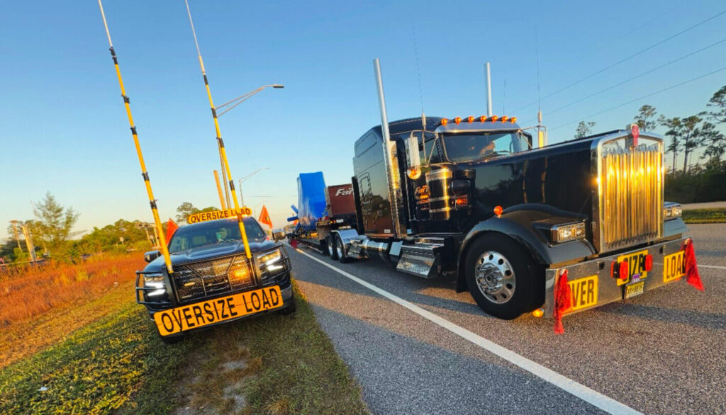 High Pole Pilot Car by Angelo's Transportation, next to a Semi Truck with a heavy load