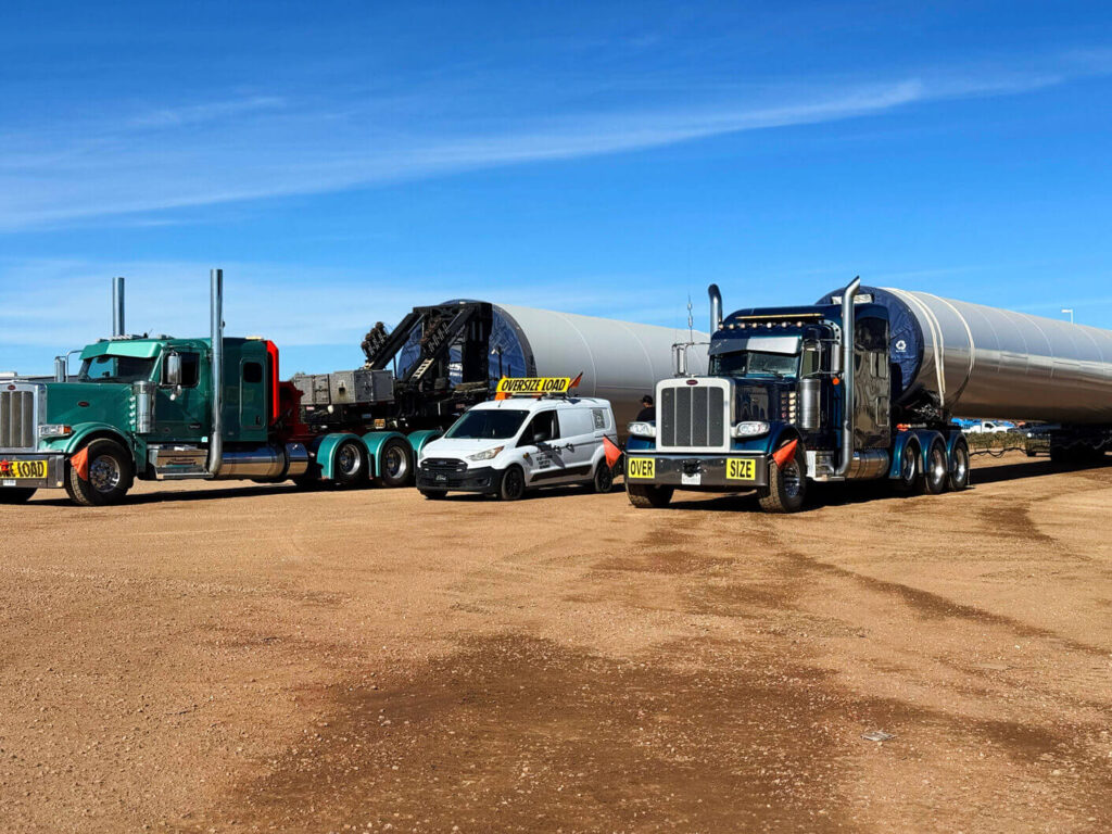 2 semi trucks with angelos transportation pilot car on dirt road